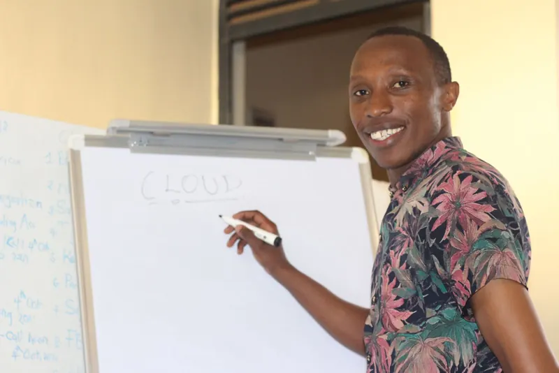 Simon Mugetha smiling as he writes CLOUD on a whiteboard